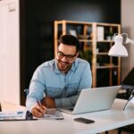 Young business man working at home with laptop and papers on desk Young business man working at home with laptop and papers on desk