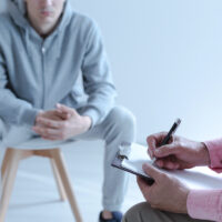 A young troubled man sitting on a chair in a blurred background.