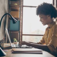 Profile side photo of smart cool afro american girl entrepreneur sit table use laptop work presentation in office loft workplace Profile side photo of smart cool afro american girl entrepreneur sit table use laptop work presentation in office loft workplace